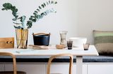 Weißer Tisch mit einer Vase und Eukalyptuszweigen, Gusseisentopf und Holzstühlen