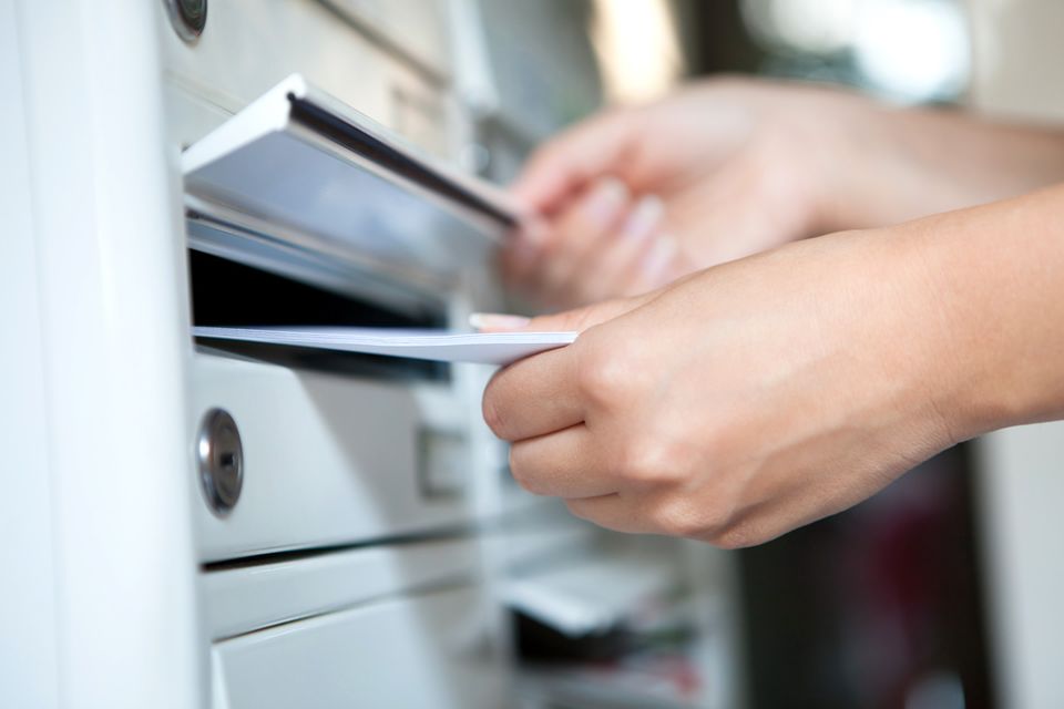 Eine Hand wirft mehrere Briefe in einen Briefkasten