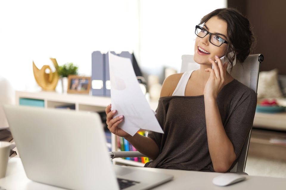 Attraktive junge Frau telefoniert vorm Notebook