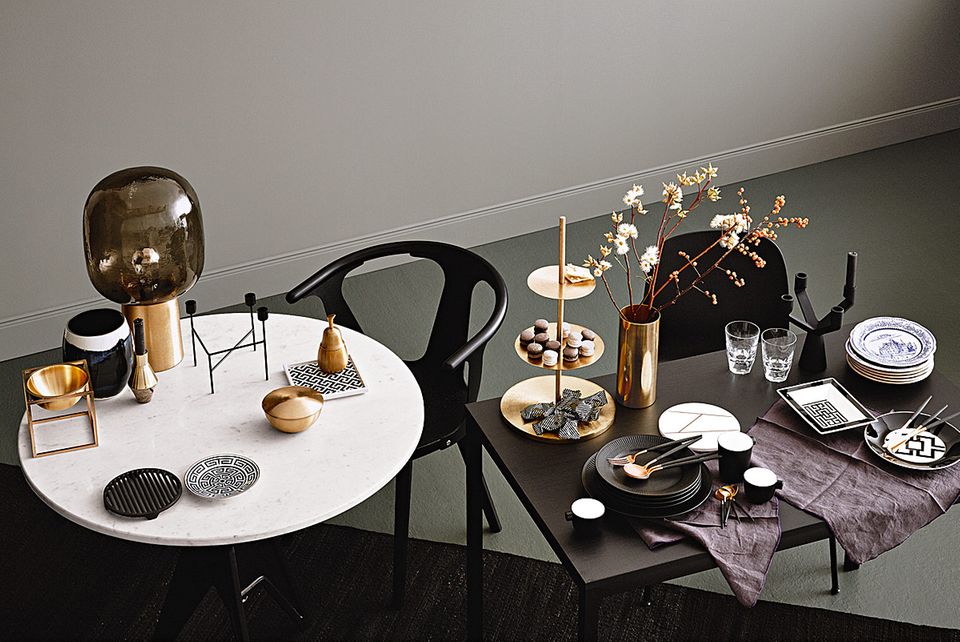 Lässig gedeckter Tisch mit Messing, Schwarz, Marmor und winterlichen Zweigen.