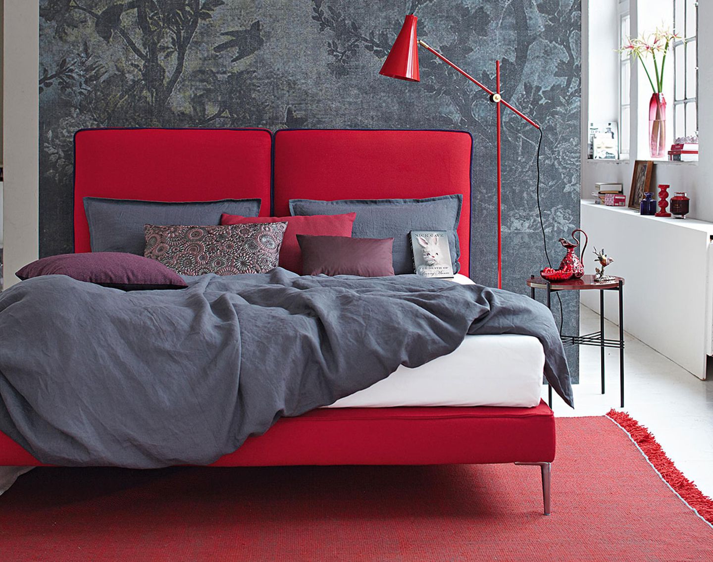 Doppelbett in Rot mit grauer Bettwäsche vor einer grauen Wand