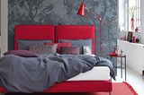 Doppelbett in Rot mit grauer Bettwäsche vor einer grauen Wand