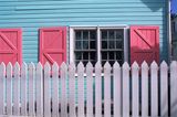 Hellblaues Haus mit rose Fensterläden und weißem Holzzaun