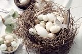 Osternest aus Zweigen mit Eiern in verschiedenen Größen auf einer Leinentischdecke