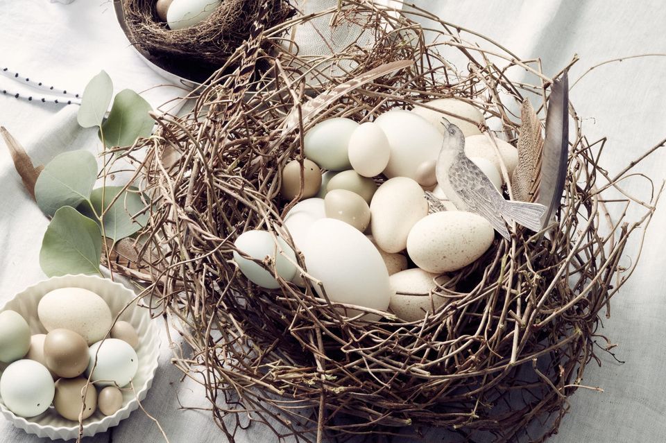 Osternest aus Zweigen mit Eiern in verschiedenen Größen auf einer Leinentischdecke