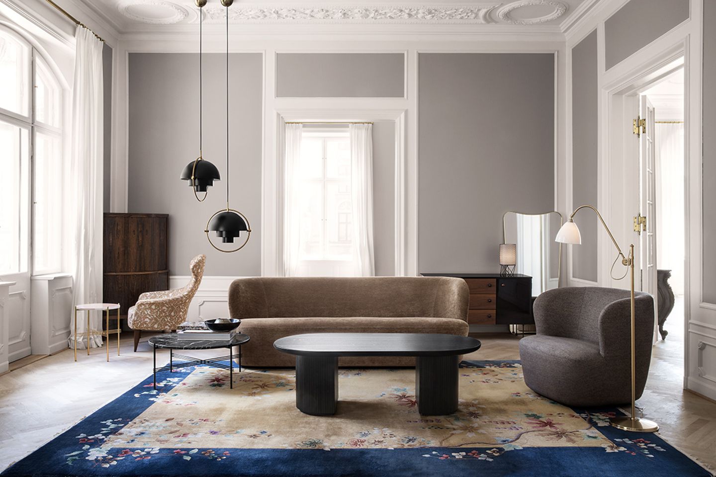 Wohnzimmer in einer Altbauwohnung mit stilvoll gestalteter Stuckdecke, grauen Wänden und Möbeln in dunklen Tönen