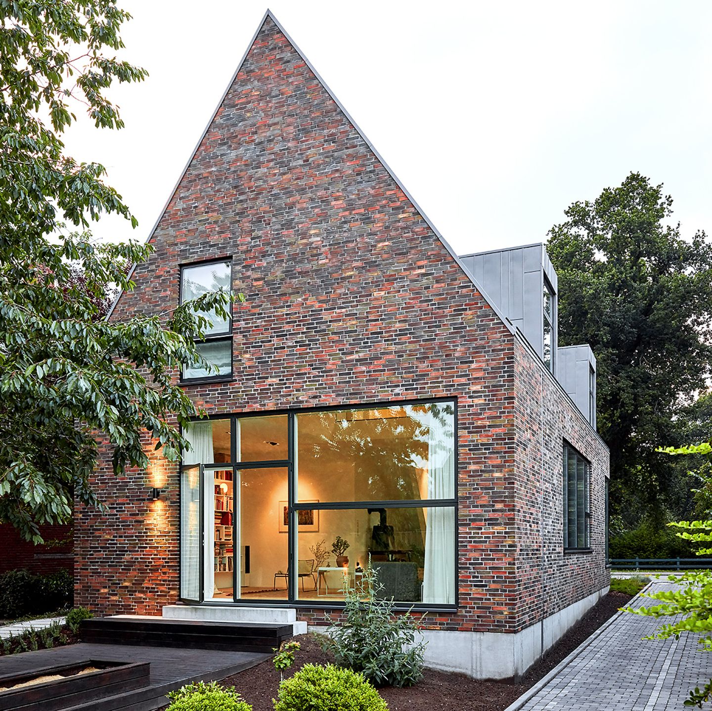 Einfamilienhaus mit Backsteinfassade, spitzem Satteldach und großem bodentiefem Fenster im Wohnzimmer
