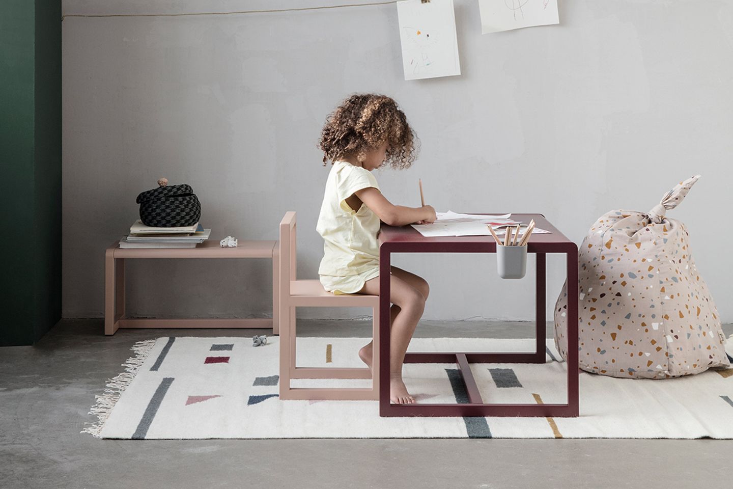 Braunhaariges, gelocktes Mädchen malt an einem Kindertisch