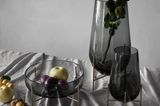 Verschiedene Schalen und Vasen aus Rauchglas auf einem Tisch mit verknitterter Tischdecke