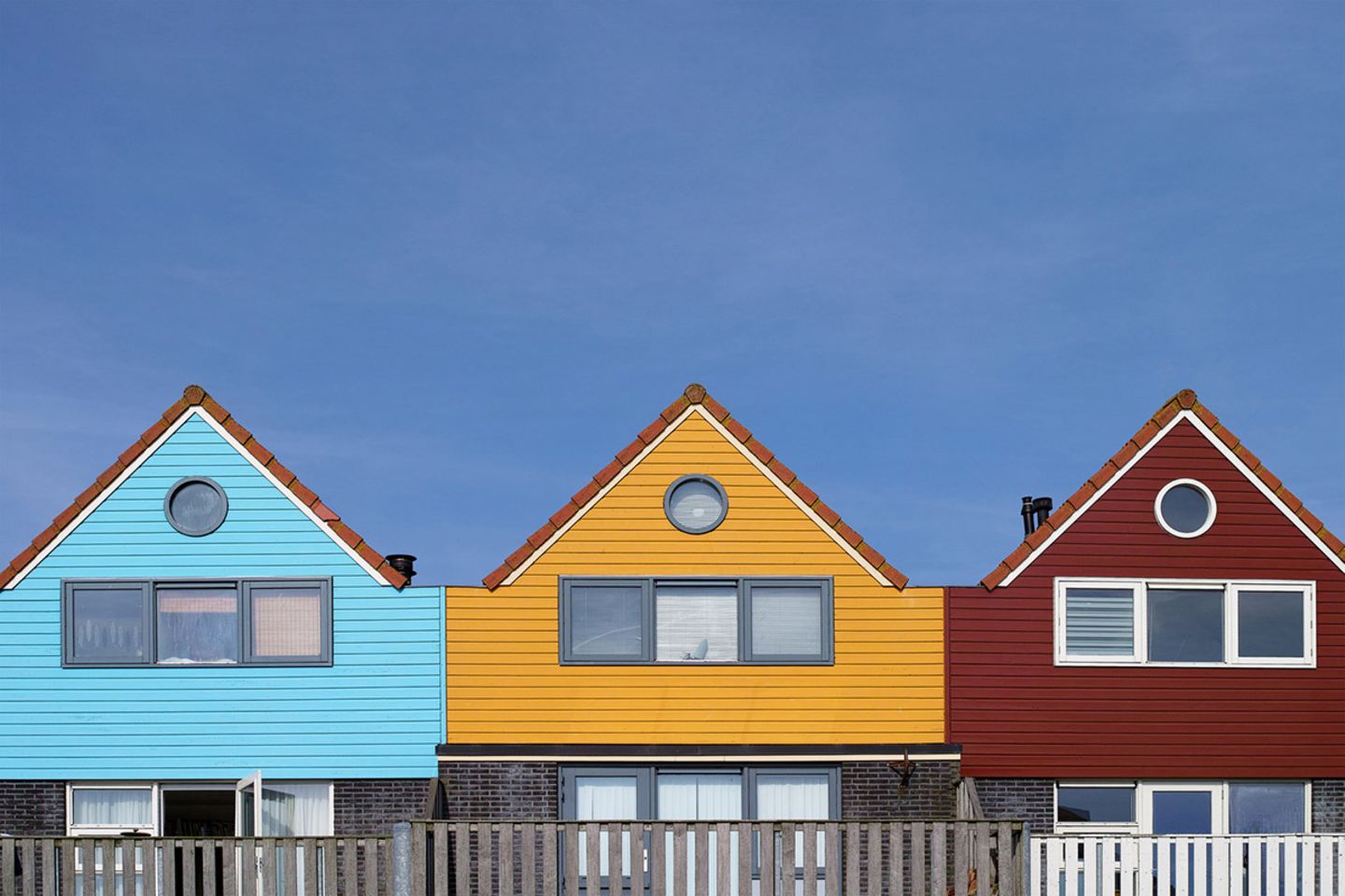 Drei Häuser in Hellblau, Gelb und Dunkelrot, die nebeneinander stehen