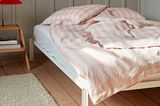 Tischleuchte "Matin" von Hay mit rotem Lampenschirm neben einem Bett mit rose-weißer Bettwäsche