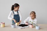 Kinder pflanzen Samen in pastellfarbenen Kunststofftöpfen