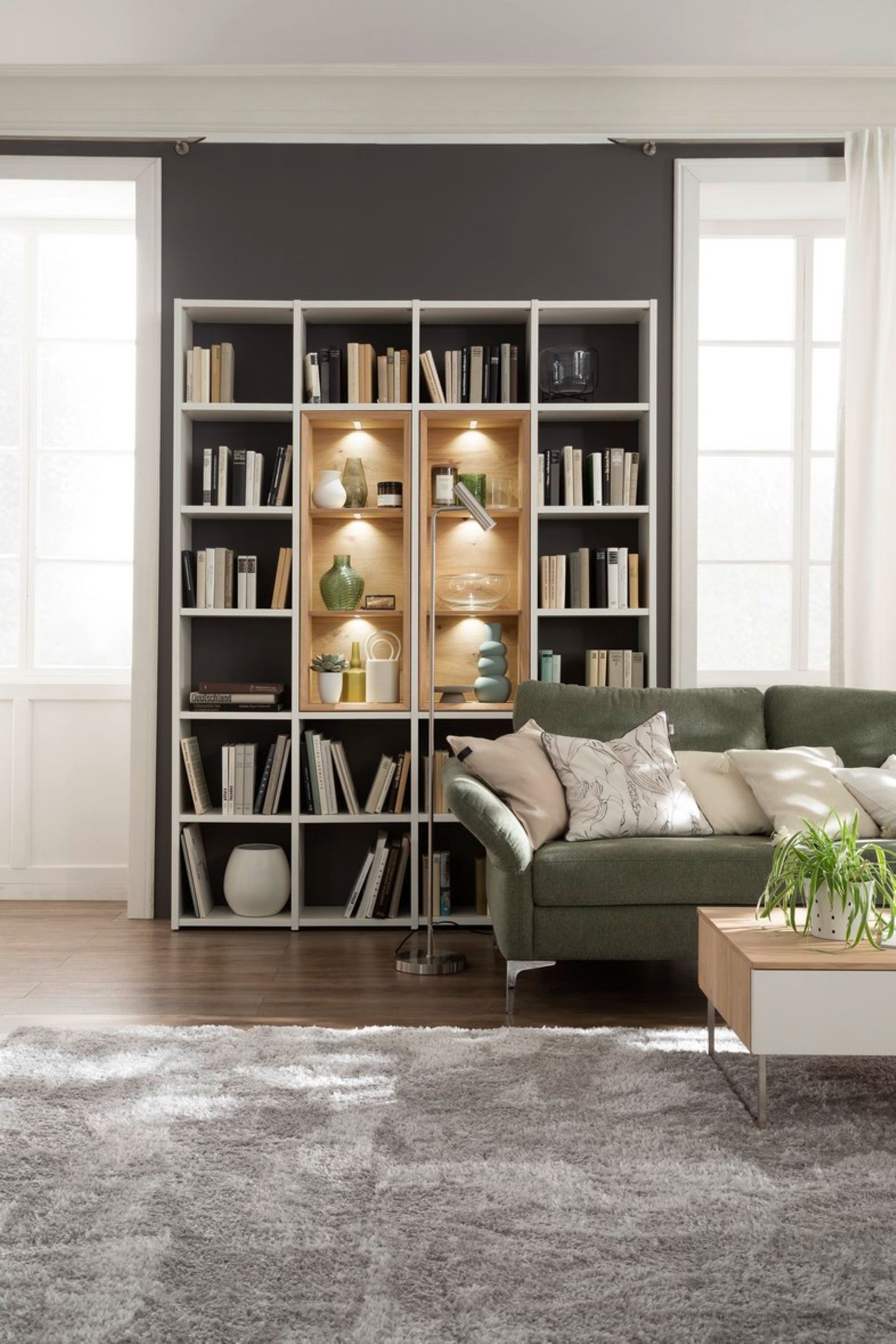 Wohnzimmer mit grünem Sofa, Bücherregal und beigefarbenem Teppich