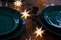 Lichterkette in Sternform auf einem festlich gedeckten Tisch mit dunkler Keramik.