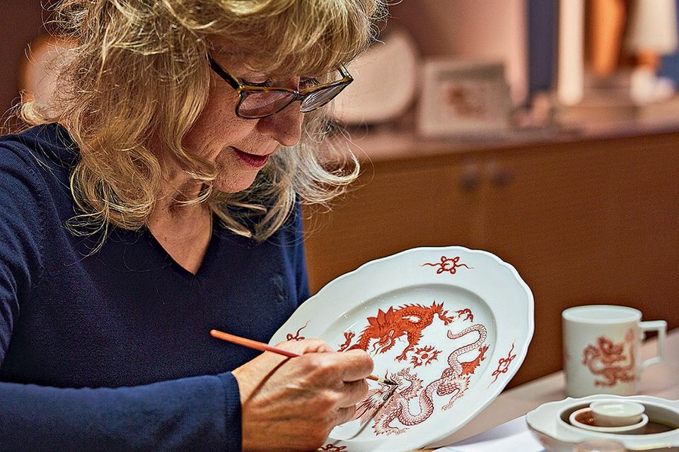 Sorgfältig trägt Christa Nettke das berühmte Ming-Drachen-Muster auf einen Teller auf Sorgfältig trägt Christa Nettke das berühmte Ming-Drachen-Muster auf einen Teller auf