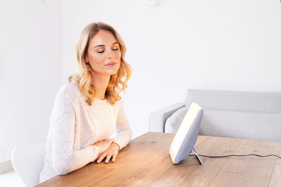 Frau sitzt am Tisch und schaut genussvoll in die Tageslichtleuchte