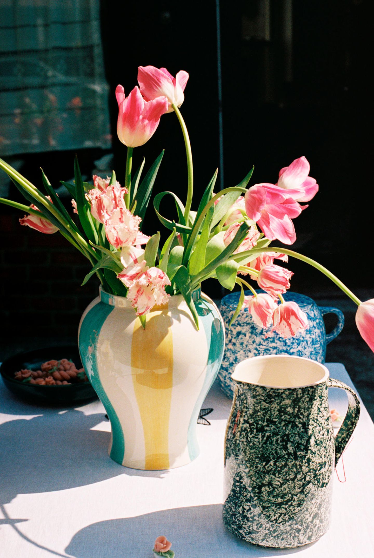 Rosefarbene Tulpen in einer Vase umgeben von Muffins und weiteren Kaffee- und Kuchenutensilien