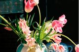 Rosefarbene Tulpen in einer Vase umgeben von Muffins und weiteren Kaffee- und Kuchenutensilien