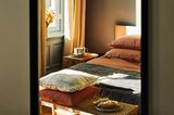 Bettwäsche in Orange und Erdtönen in einem Schlafzimmer mit großem Fenster.