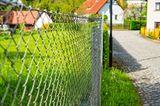 Maschendrahtzaun an einer Kopfsteinpflasterstraße in einem Dorf
