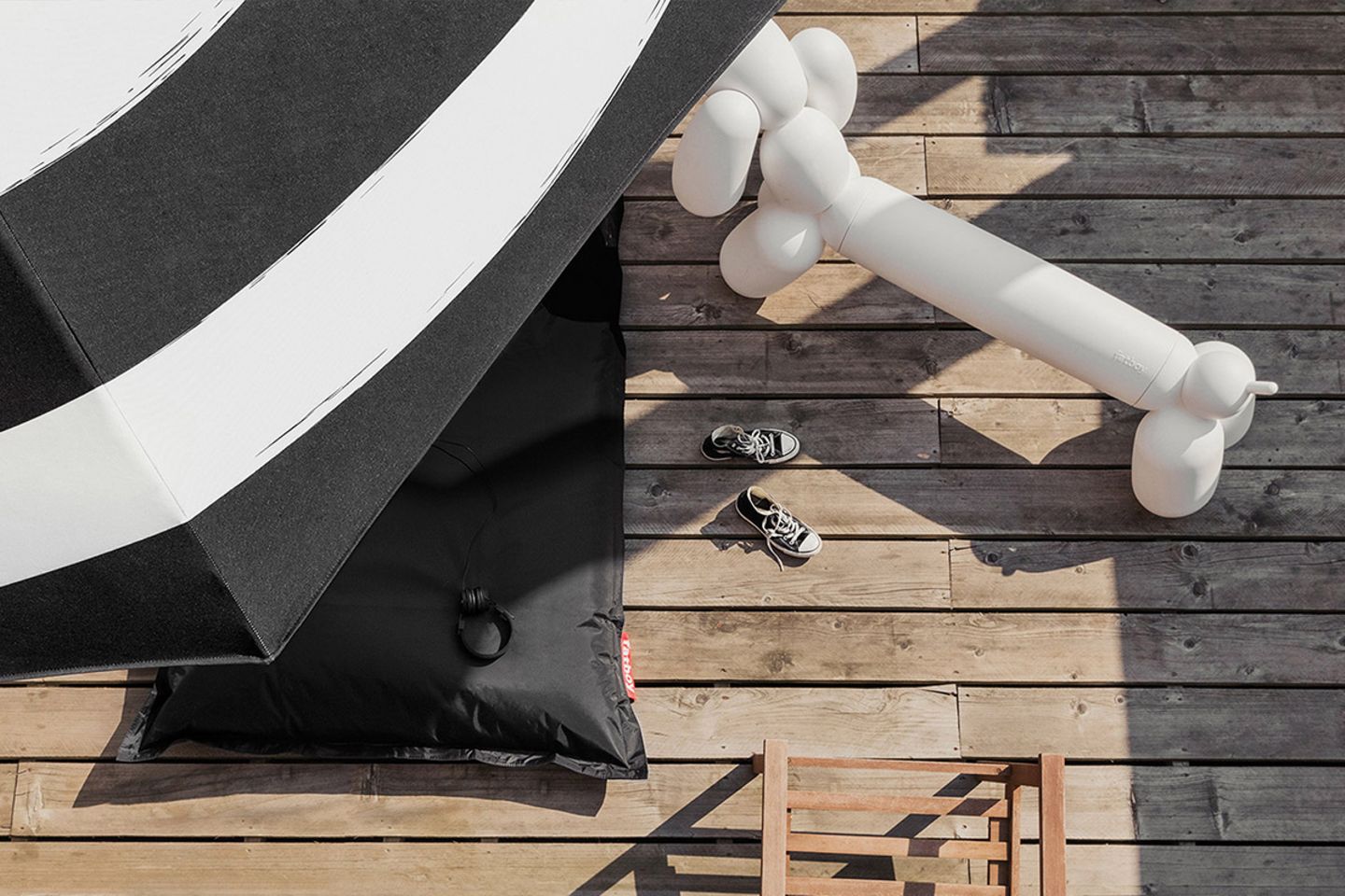 Sitzbank "Attackle" von Fatboy, die aussieht wie eine Ballonfigur in Dackelform, neben einem schwarzen Sitzsack und einem Sonne…