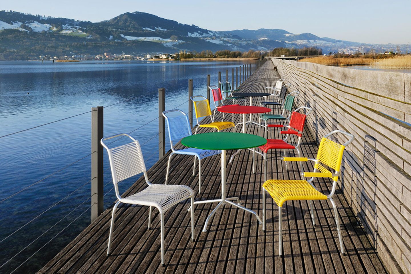 Gartenstühle und Tische "Haefeli" in zahlreichen bunten Farben auf einem Steg an einem See mit Bergpanorama