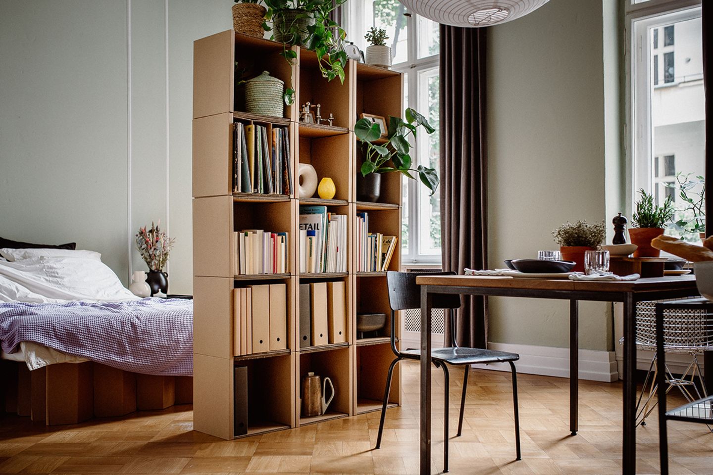 Bücherregal aus Wellpappe als Raumteiler zwischen Bett und Esstisch