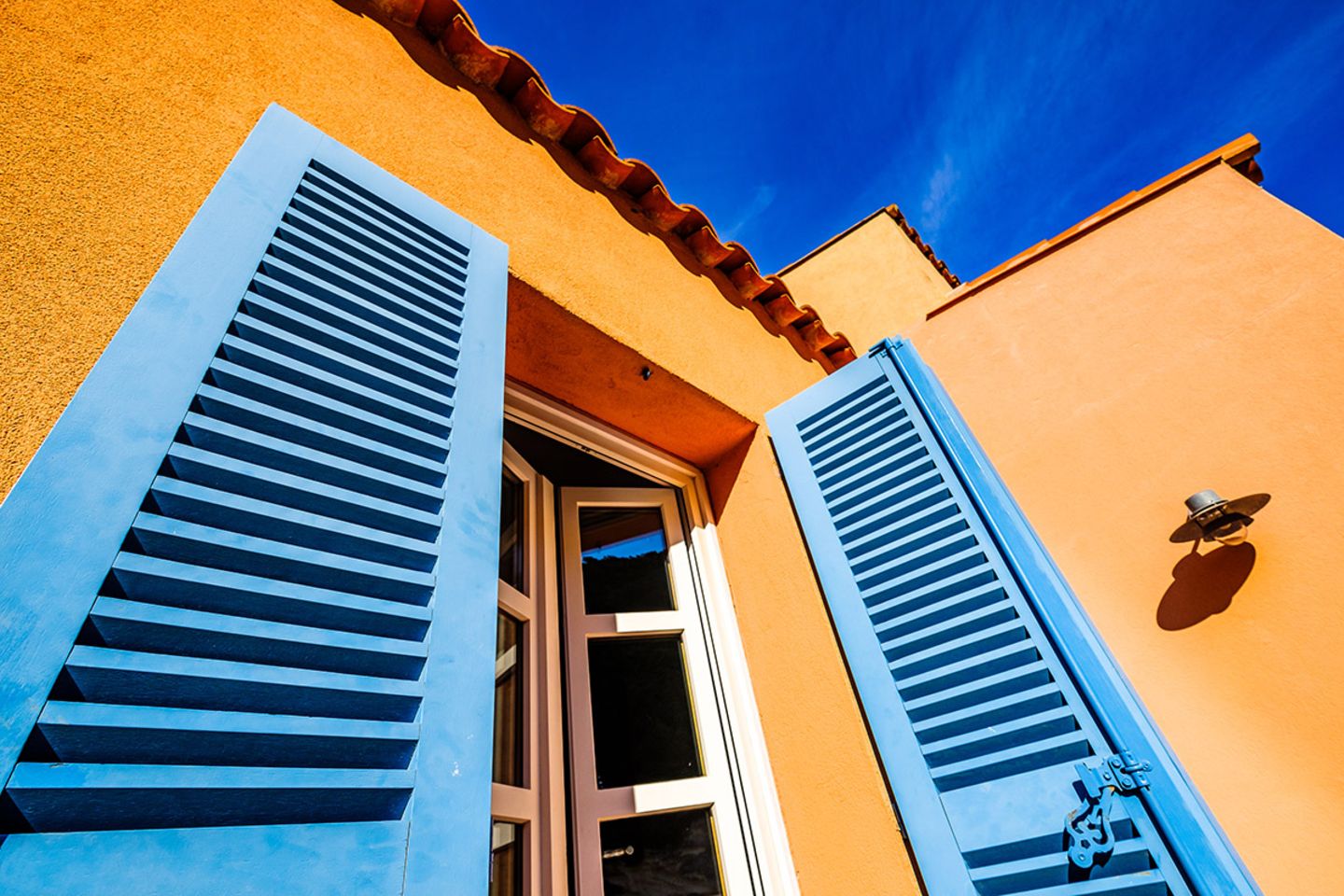 Orangefarbene Hausfassade mit hellblauen Fensterläden