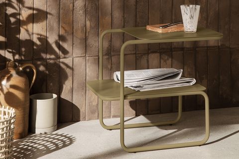Doppelstöckiger Beistelltisch "Level" von Ferm Living in Oliv vor einer Steinmauer