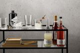 Gläser, Eiswürfel in einer Glasschale sowie verschiedene alkoholische Getränke auf einem Barwagen