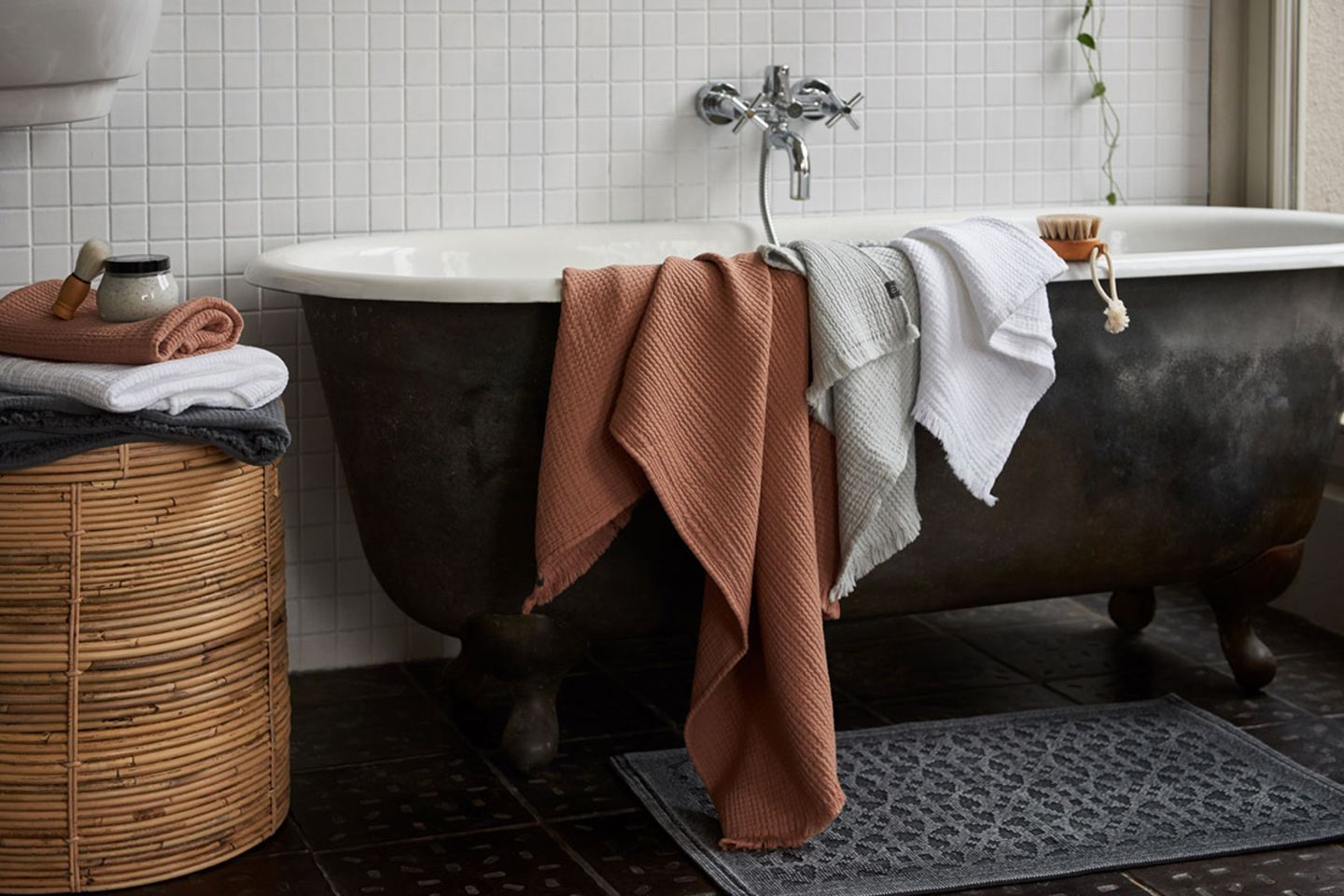 Musselin-Handtücher in Terracotta und Grau auf dem Rand einer Badewanne liegend
