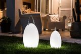 Zwei tragbare, leuchtende Designlampen im Gras vor einer Terrasse