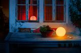 Warmweiß leuchtende Kugellampe auf einem Gartentisch vor Hausfassade