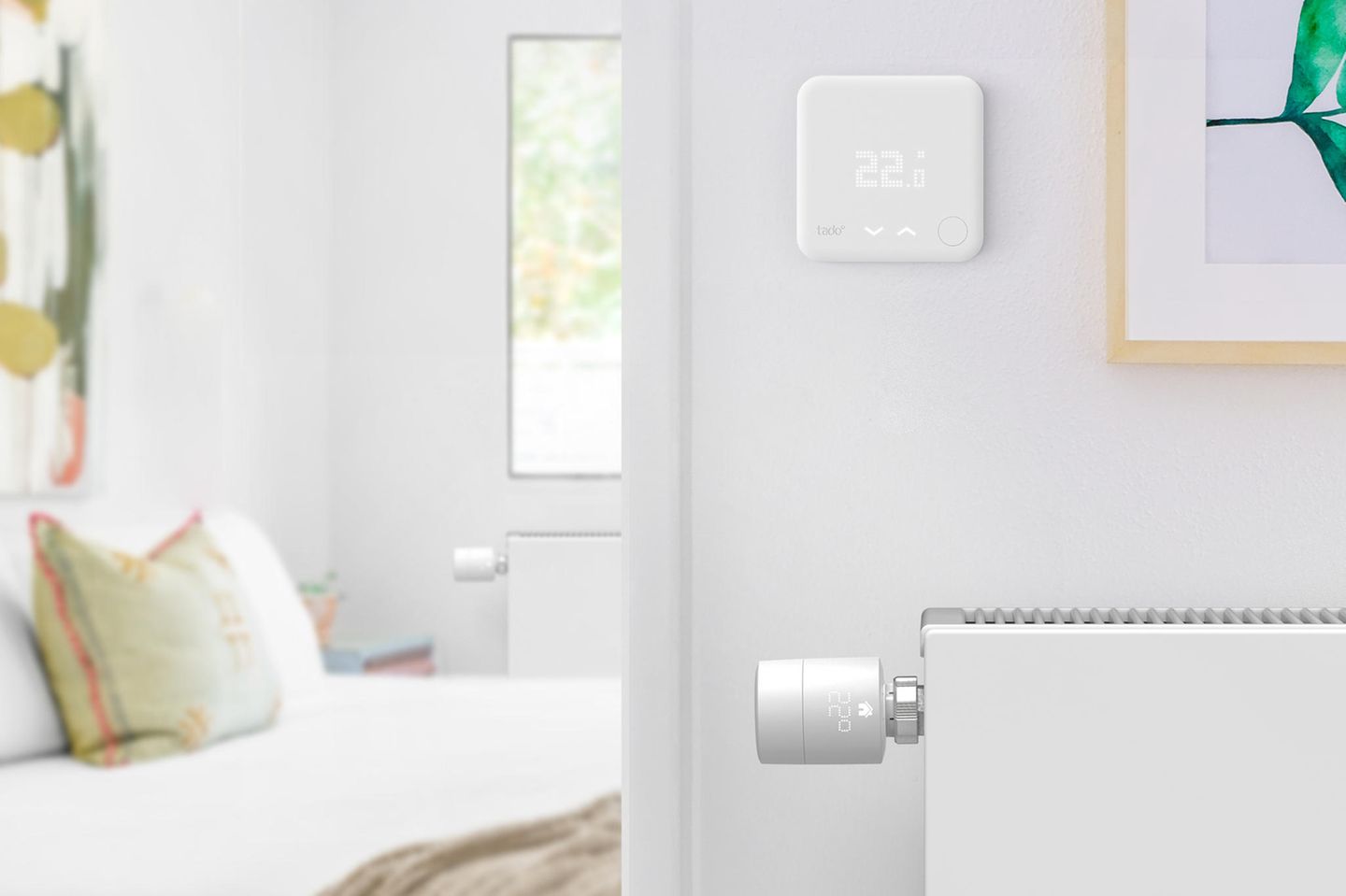 Smartes Thermostat an einem weißen Heizkörper im Flur vor einem geöffneten Schlafzimmer