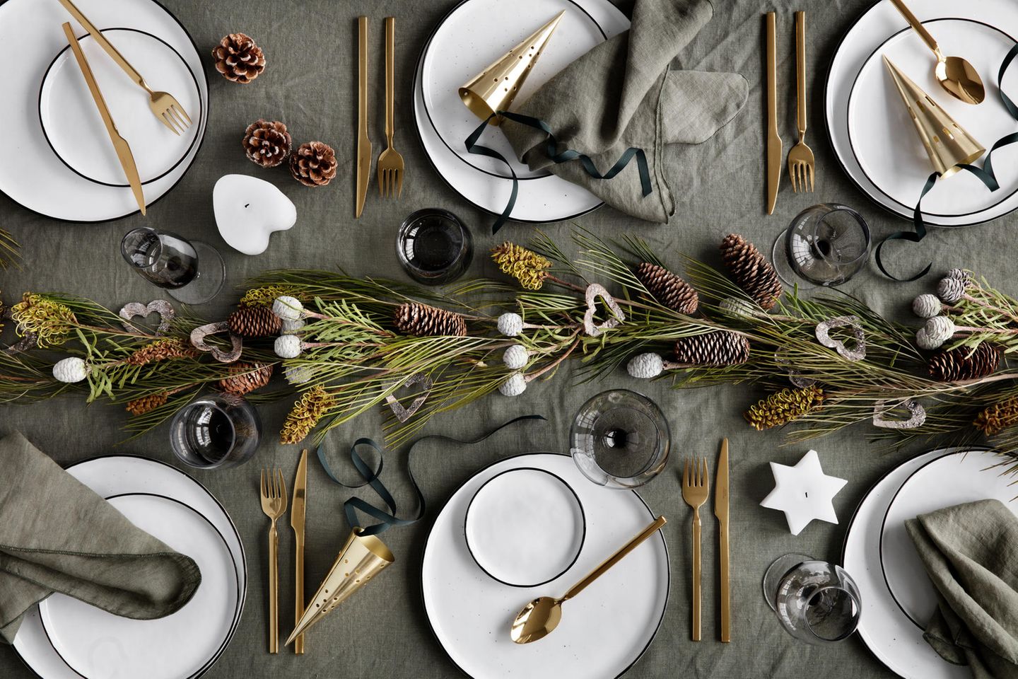 Weihnachtlich dekorierter Tisch mit hellem Geschirr, goldenem Besteck und Tannengesteck