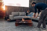 Mann grillt über Feuerschale, Frau auf Outdoor-Sofa