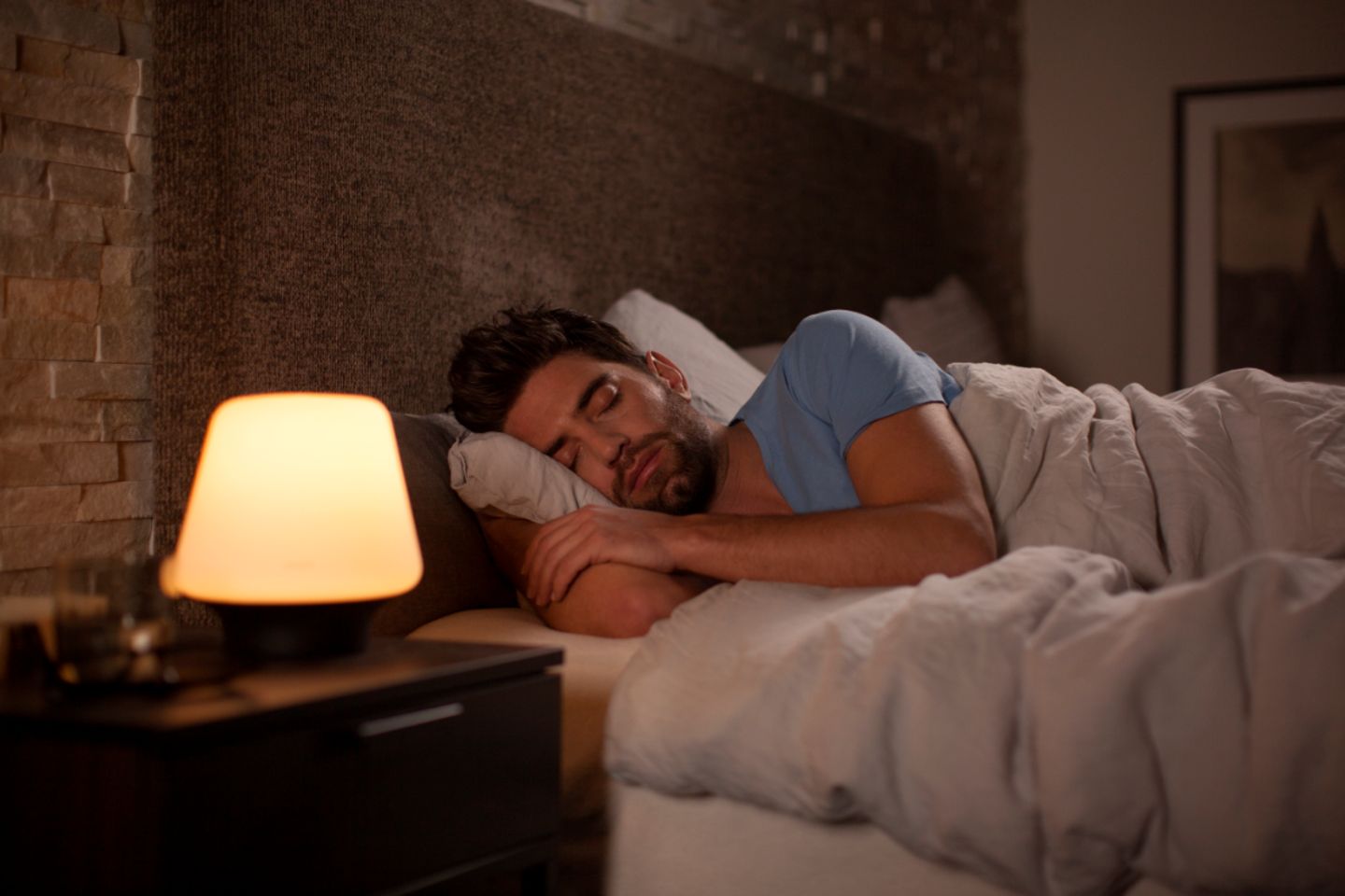 Schlafender Mann in einem Bett neben sanft beleuchtetem Nachttisch