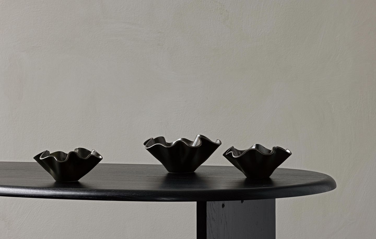 Drei schwarze, wellenförmige Dekoschalen auf schwarzem Tisch