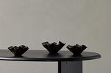 Drei schwarze, wellenförmige Dekoschalen auf schwarzem Tisch