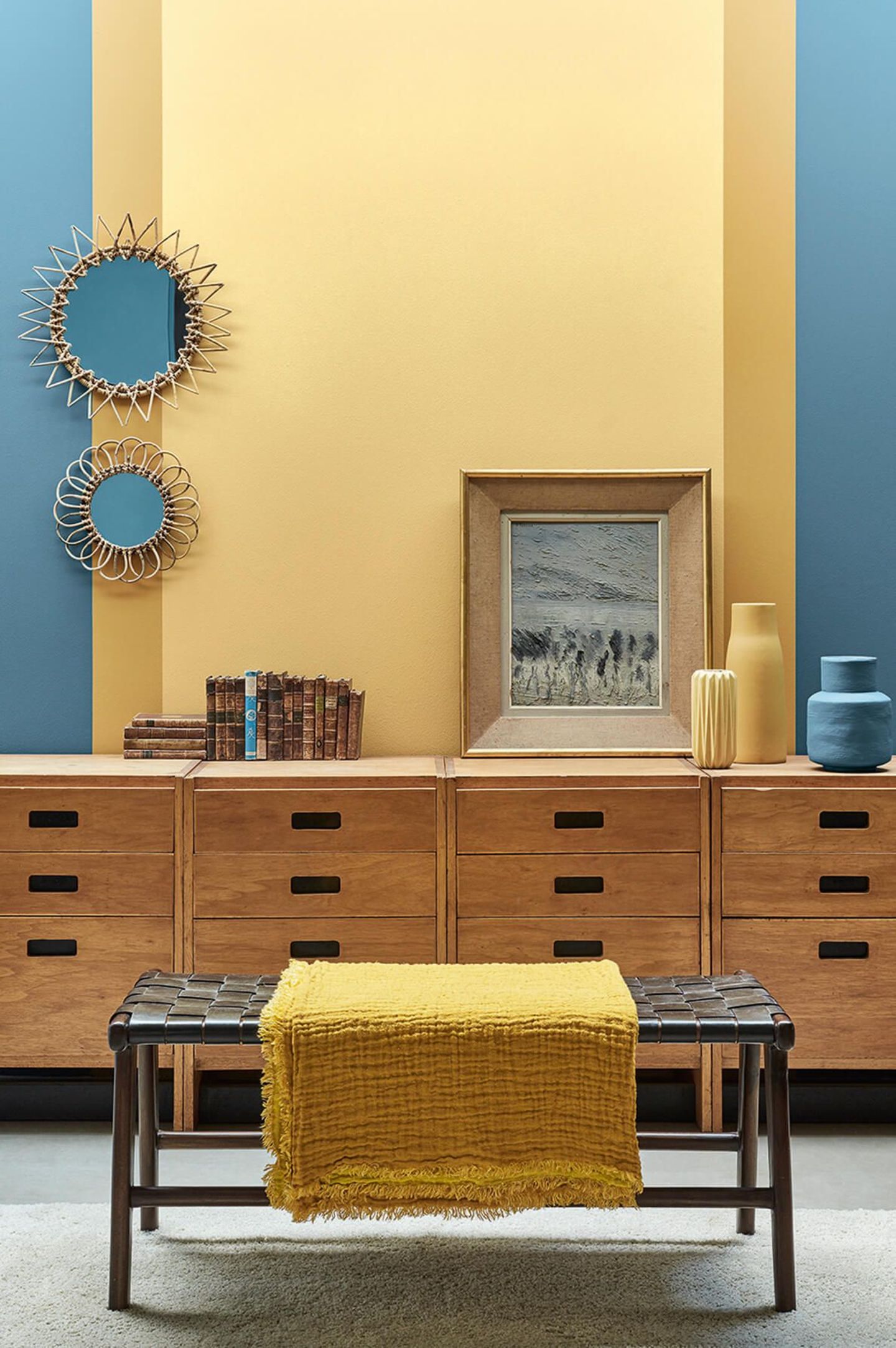 Gelbes Rechteck mit senfgelben Streifen an einer Wand in Blau mit Holzmöbeln im Vordergrund