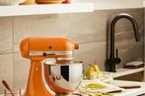 Küchenmaschine Kitchenaid in leuchtendem Orange in einer Küche in Sand- und Brauntönen