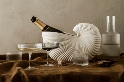 Muschelförmiger Kübel mit Chamapgnerflasche und -gläsern auf erdfarbener Tischdecke