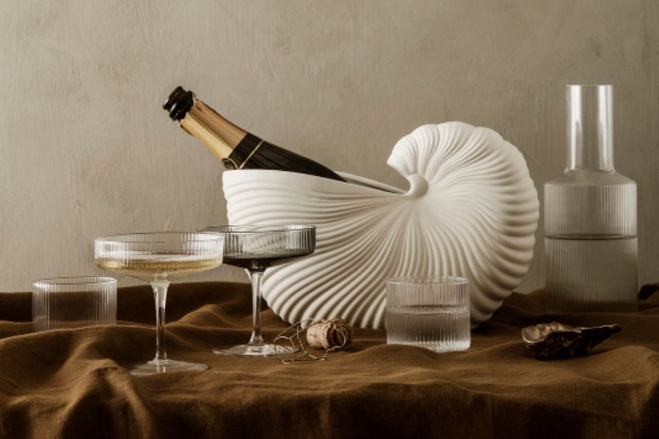 Muschelförmiger Kübel mit Chamapgnerflasche und -gläsern auf erdfarbener Tischdecke