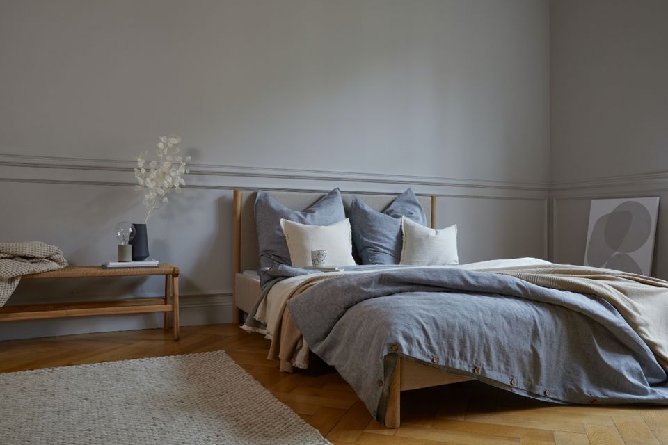Schlafzimmer mit Parkett, grauen Kassettenwänden und Bettwäsche in Graublau