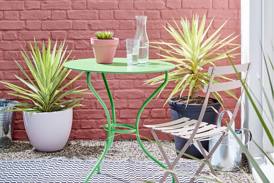 Klappstuhl und grüner Gartentisch mit Pflanzenkübeln vor rosafarbener Wand