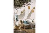 Helle Gartenmöbel mit hängenden Korbleuchten vor weißer Wand