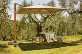 Sonnenschirm mit seitlichem Ständer über einem Gartentisch und mehreren Bänken mitten auf einer Wiese
