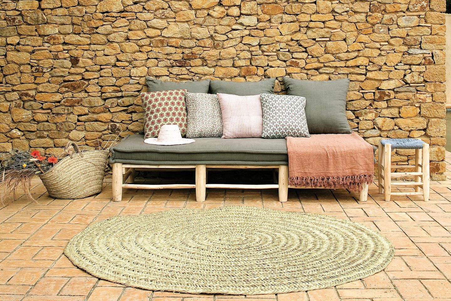 Outdoorsofa mit Kissen in verschiedenen Mustern und einem Outdoor-Teppich vor einer Steinwand