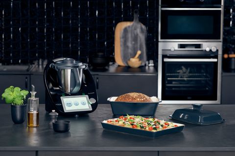 Thermomix in Schwarz auf dunkler Kücheninsel mit Pizza und Brot