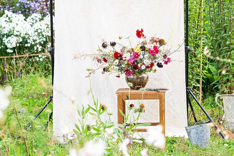 Blumen-Arrangement auf einem kleinen Holztisch vor einer weißen Leinwand im Grünen